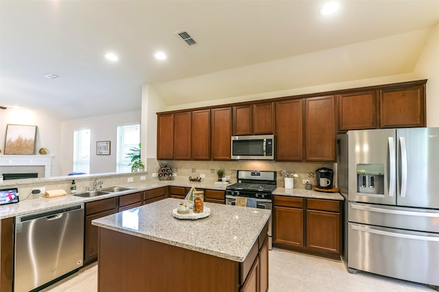 kitchen featuring appliances with stainless steel finishes, backsplash, light stone countertops, a kitchen island, and sink