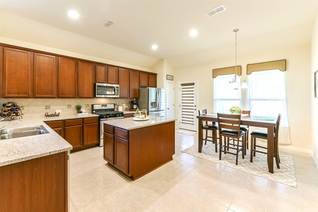 kitchen featuring a kitchen island, sink, hanging light fixtures, light stone countertops, and stainless steel appliances