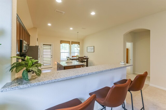 kitchen featuring pendant lighting, appliances with stainless steel finishes, a kitchen island, kitchen peninsula, and light stone counters