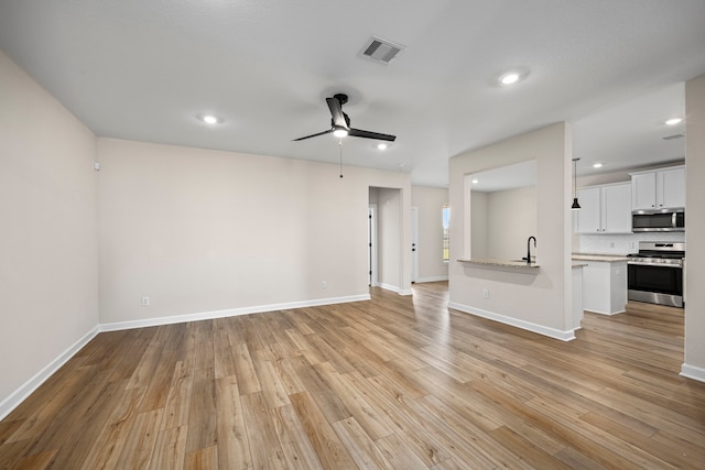 unfurnished living room featuring ceiling fan, light wood-type flooring, and sink