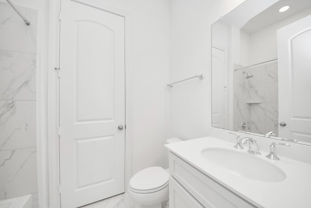 bathroom with toilet, a tile shower, and vanity