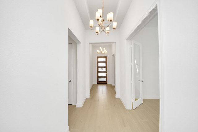 hallway featuring light wood-type flooring, french doors, and an inviting chandelier