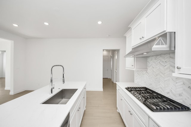 kitchen with stainless steel gas stovetop, white cabinetry, light hardwood / wood-style floors, backsplash, and sink