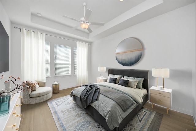 bedroom with ceiling fan, dark wood-type flooring, and a tray ceiling