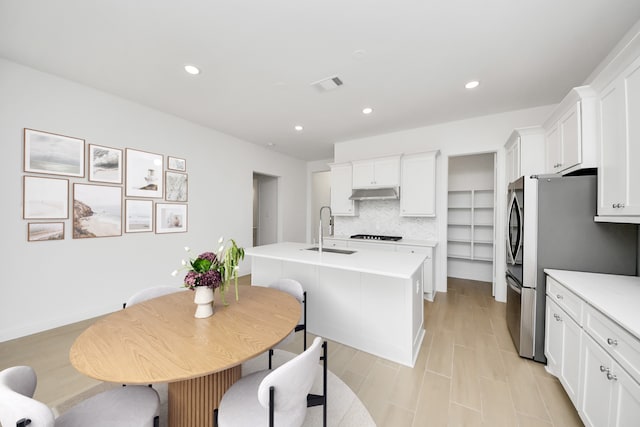 kitchen featuring an island with sink, black gas cooktop, backsplash, white cabinets, and sink