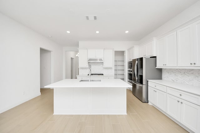 kitchen featuring backsplash, sink, white cabinetry, a kitchen island with sink, and appliances with stainless steel finishes