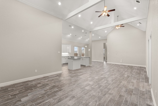 unfurnished living room with ceiling fan, sink, high vaulted ceiling, and crown molding