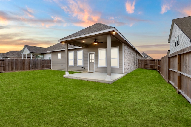 back house at dusk featuring ceiling fan, a lawn, and a patio area