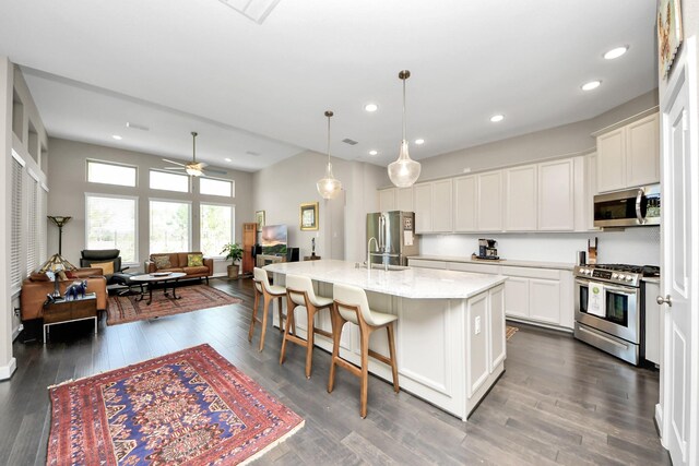 kitchen featuring decorative light fixtures, white cabinetry, stainless steel appliances, a kitchen island with sink, and ceiling fan