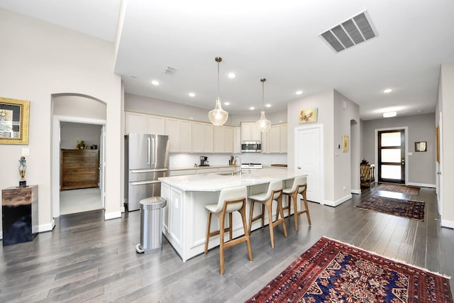 kitchen featuring pendant lighting, stainless steel appliances, an island with sink, sink, and a breakfast bar