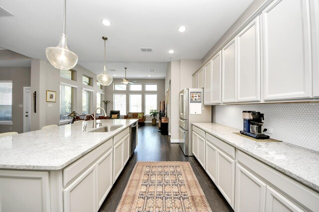 kitchen with light stone countertops, sink, hanging light fixtures, and an island with sink