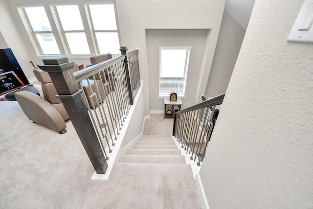 staircase with a healthy amount of sunlight, baseboards, carpet flooring, and a textured wall