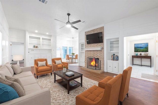 living room featuring a brick fireplace, ceiling fan, light hardwood / wood-style flooring, and built in shelves