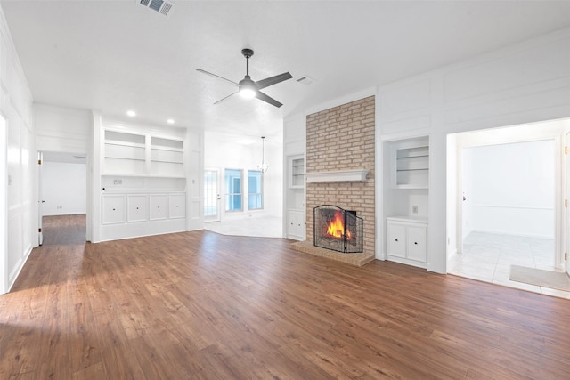 unfurnished living room with ceiling fan, built in shelves, a brick fireplace, and hardwood / wood-style floors