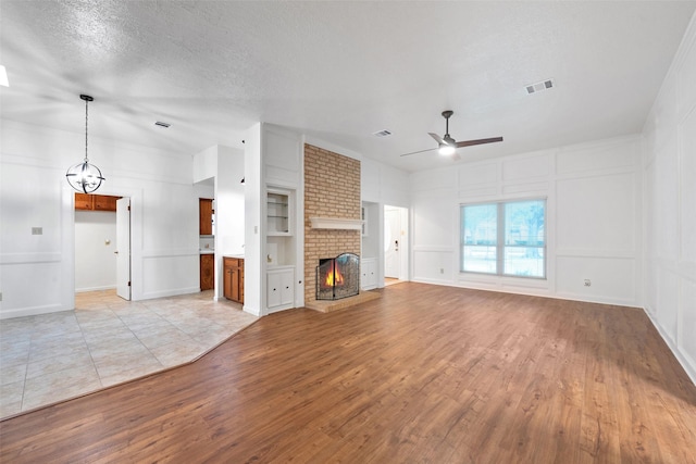 unfurnished living room with ceiling fan, built in shelves, a fireplace, and light hardwood / wood-style flooring