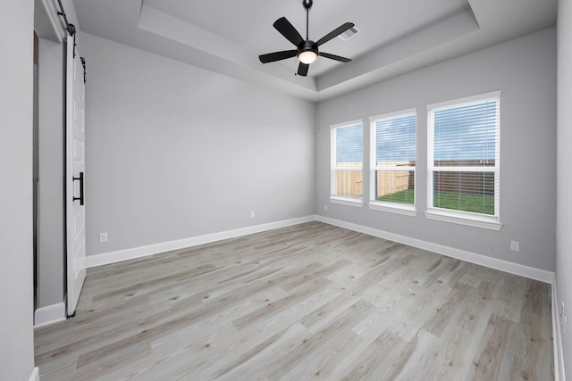 spare room with a raised ceiling, a barn door, and light hardwood / wood-style flooring