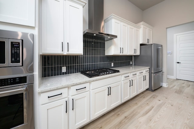 kitchen featuring stainless steel appliances, tasteful backsplash, light stone countertops, white cabinets, and wall chimney range hood