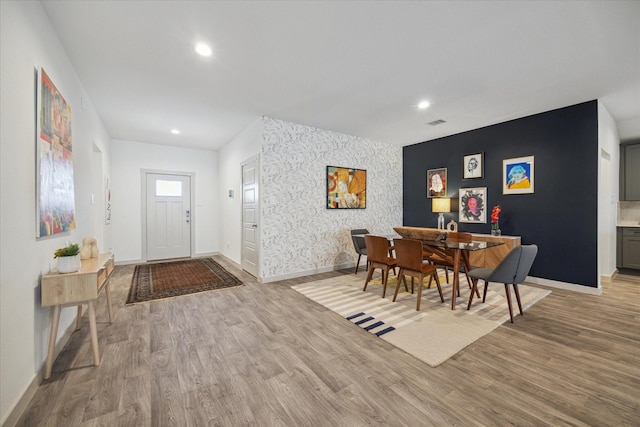 dining space with light wood-style floors, an accent wall, baseboards, and wallpapered walls