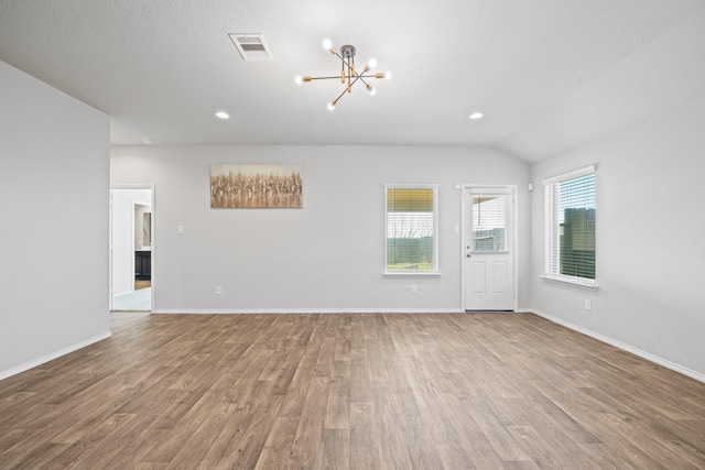 empty room featuring lofted ceiling, wood-type flooring, and an inviting chandelier