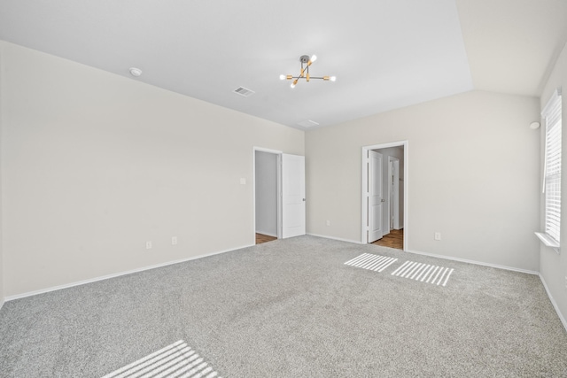 carpeted spare room featuring an inviting chandelier and lofted ceiling