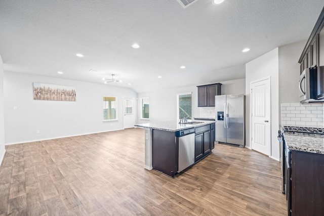 kitchen with stainless steel appliances, decorative backsplash, a center island with sink, and light stone countertops