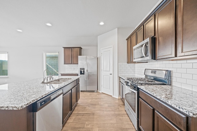 kitchen featuring appliances with stainless steel finishes, decorative backsplash, a kitchen island with sink, light wood-type flooring, and sink