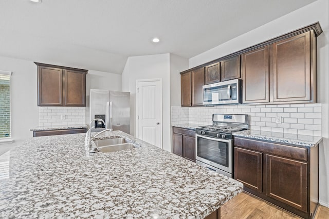 kitchen with sink, a center island with sink, stainless steel appliances, and tasteful backsplash