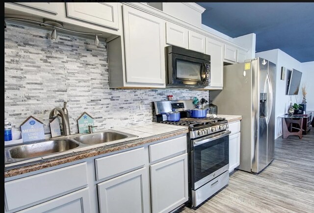 kitchen featuring light hardwood / wood-style floors, stainless steel appliances, backsplash, white cabinets, and sink