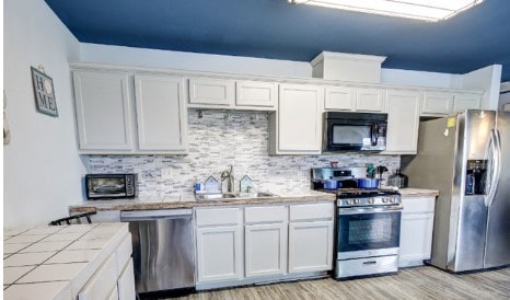 kitchen with sink, tile countertops, white cabinets, and appliances with stainless steel finishes