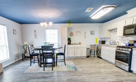 kitchen with hanging light fixtures, plenty of natural light, stainless steel range with gas stovetop, and white cabinets