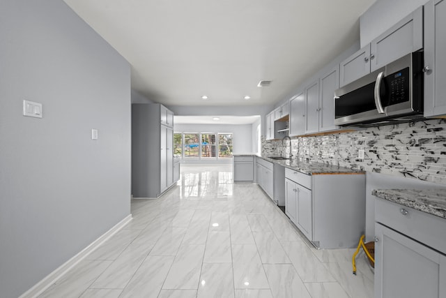 kitchen with appliances with stainless steel finishes, tasteful backsplash, sink, gray cabinets, and light stone counters