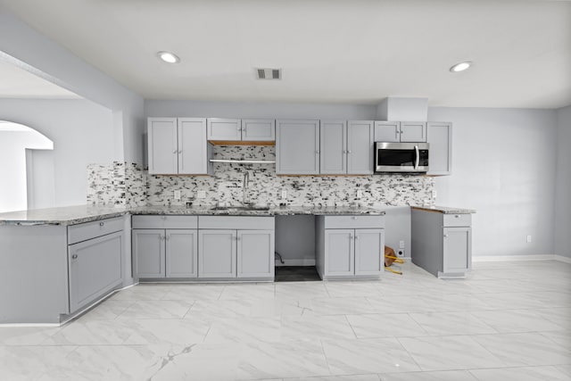 kitchen with decorative backsplash, gray cabinetry, kitchen peninsula, and sink