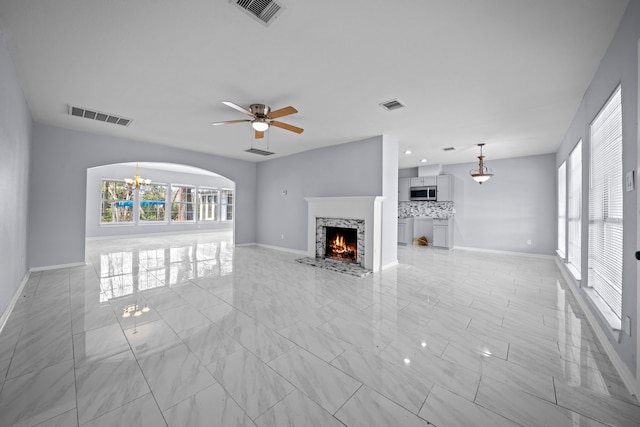 unfurnished living room featuring ceiling fan with notable chandelier and plenty of natural light