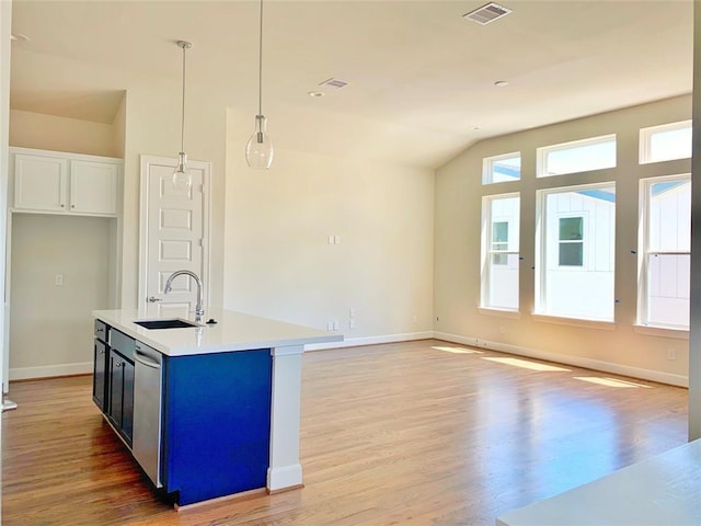 kitchen with an island with sink, vaulted ceiling, pendant lighting, white cabinets, and sink