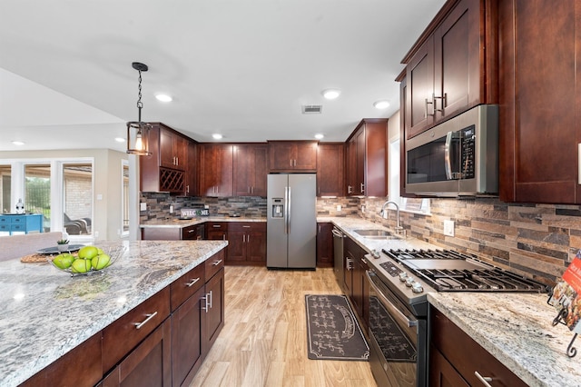 kitchen with light stone counters, sink, hanging light fixtures, and stainless steel appliances