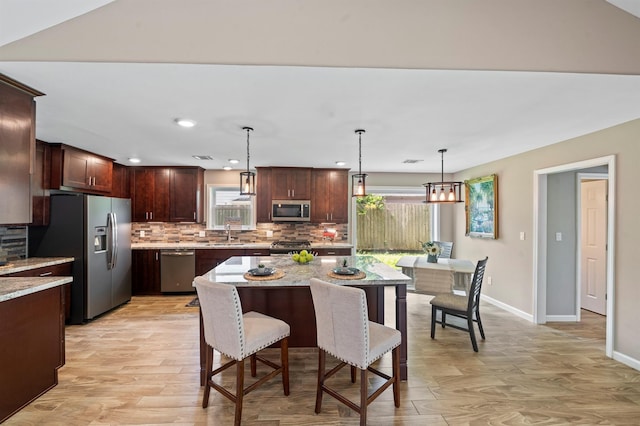 kitchen with stainless steel appliances, plenty of natural light, pendant lighting, light stone counters, and a center island