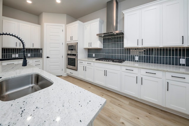 kitchen featuring white cabinetry, stainless steel appliances, decorative backsplash, light stone countertops, and wall chimney range hood