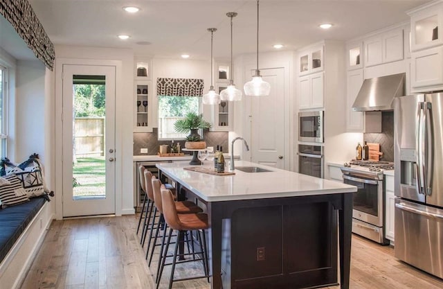 kitchen featuring sink, appliances with stainless steel finishes, a center island with sink, and wall chimney exhaust hood