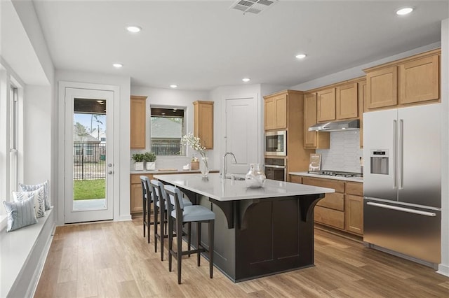 7462 Cattail Falls Ln, Porter, TX 77365 - kitchen with built in appliances, under cabinet range hood, light wood finished floors, tasteful backsplash, and recessed lighting