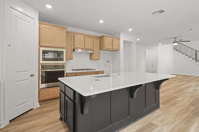 7462 Cattail Falls Ln, Porter, TX 77365 - kitchen with stainless steel appliances, under cabinet range hood, light countertops, light wood-style floors, and backsplash