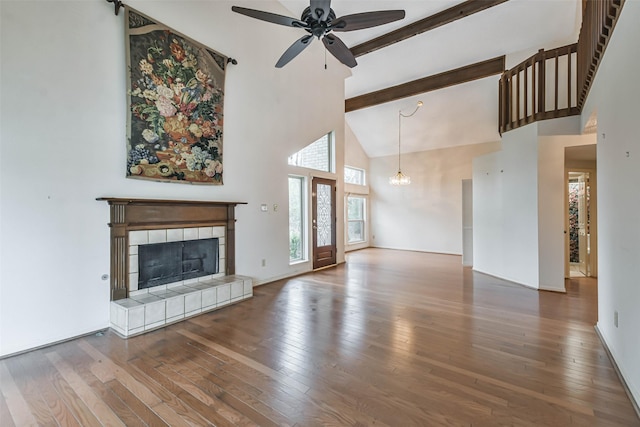 unfurnished living room with ceiling fan with notable chandelier, wood-type flooring, beamed ceiling, high vaulted ceiling, and a tiled fireplace