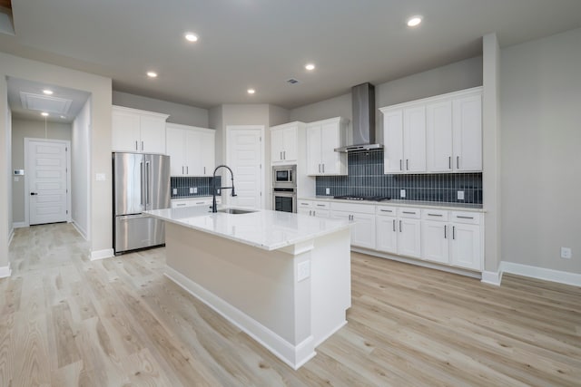 kitchen with white cabinets, wall chimney exhaust hood, stainless steel appliances, an island with sink, and sink