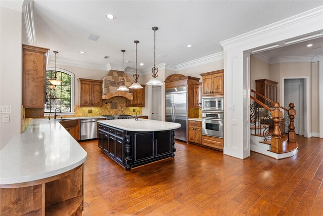 kitchen featuring decorative backsplash, a kitchen island with sink, custom range hood, pendant lighting, and built in appliances