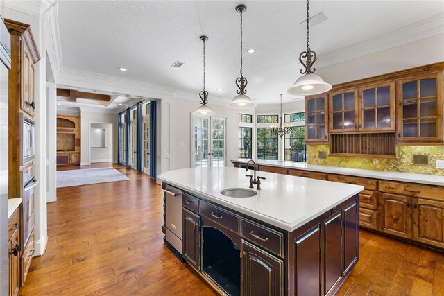 kitchen with decorative backsplash, sink, crown molding, hanging light fixtures, and an island with sink