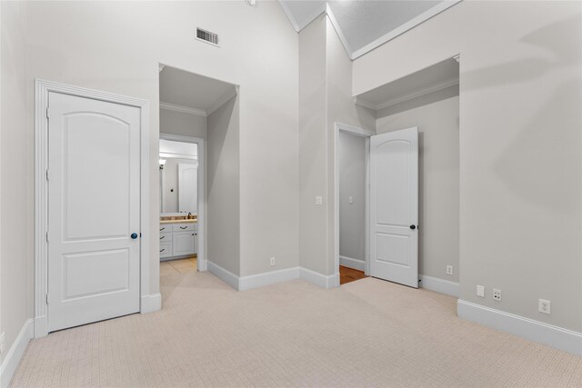 unfurnished bedroom featuring light carpet, ensuite bathroom, and ornamental molding