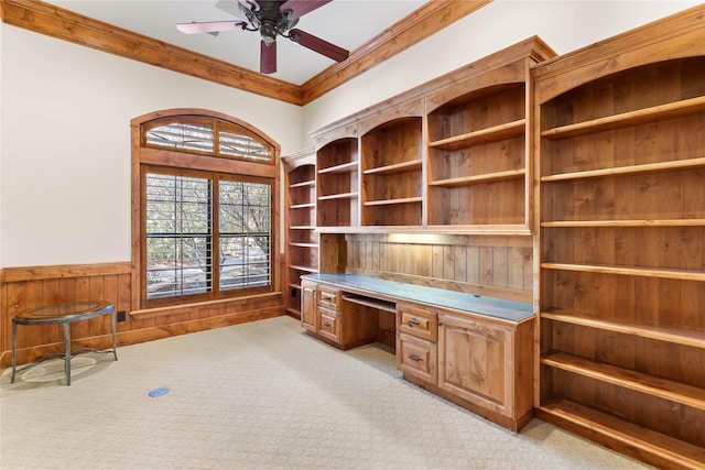 unfurnished office with ceiling fan, built in desk, light colored carpet, and wooden walls