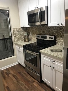 kitchen featuring dark hardwood / wood-style floors, decorative backsplash, stainless steel appliances, white cabinets, and light stone counters