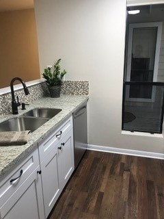 kitchen with dark wood-type flooring, stainless steel dishwasher, white cabinets, light stone counters, and sink