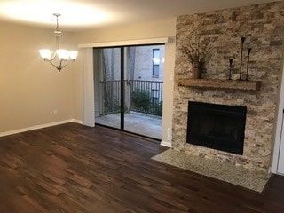 unfurnished living room featuring a notable chandelier, dark hardwood / wood-style flooring, and a stone fireplace