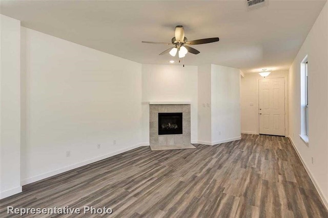 unfurnished living room with ceiling fan, a tiled fireplace, and dark wood-type flooring